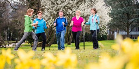 Patienten wandern mit Nordic Walking Stöcken durch den blühenden Park