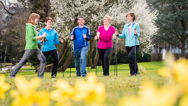 Patienten wandern mit Nordic Walking Stöcken durch den blühenden Park