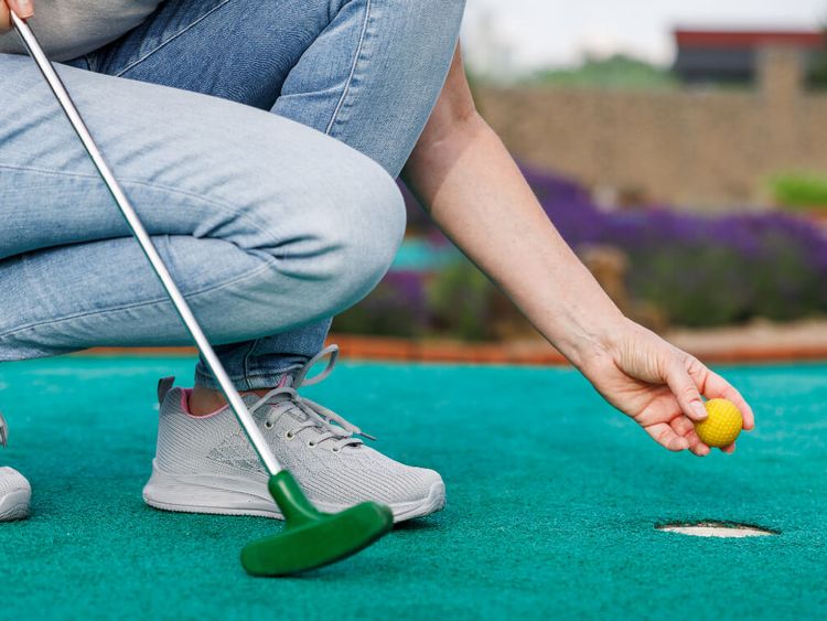 Frau kniet am Loch mit Fahne auf einem Golfplatz