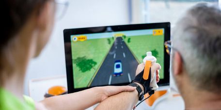 Patient trainiert seine Motorik mit einer Armschiene am Bildschirm