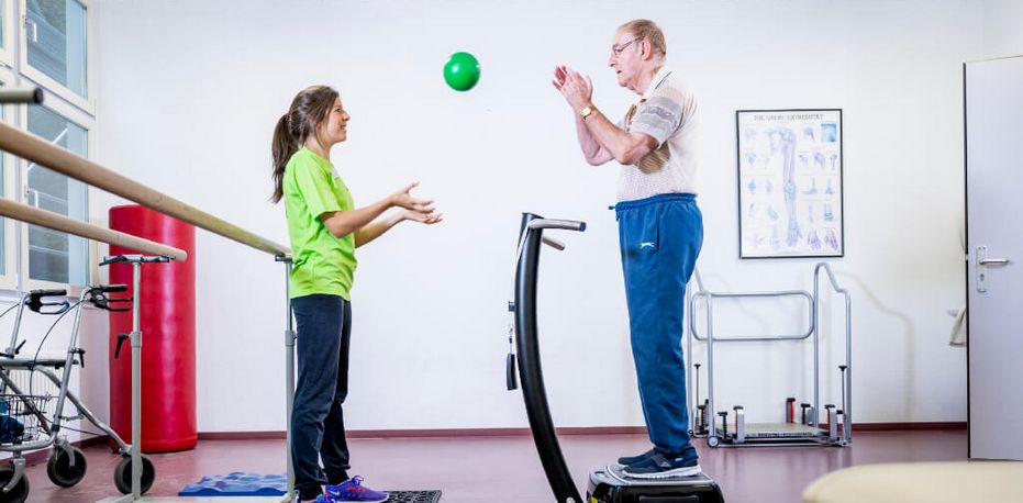 Therapeutin wirft Patienten Ball zu beim Gleichgewichtstraining
