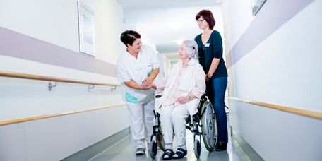 Pflegekräfte schieben eine Patientin im Rollstuhl