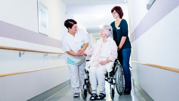 Pflegekräfte schieben eine Patientin im Rollstuhl
