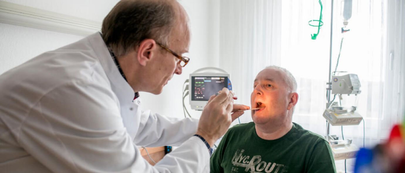 Arzt schaut in den Rachen eines Patienten