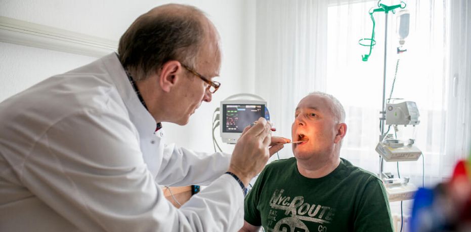 Arzt schaut in den Rachen eines Patienten